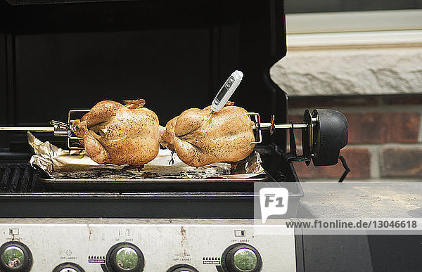 Meat thermometer inserted in chicken tandoori grilling on barbecue grill