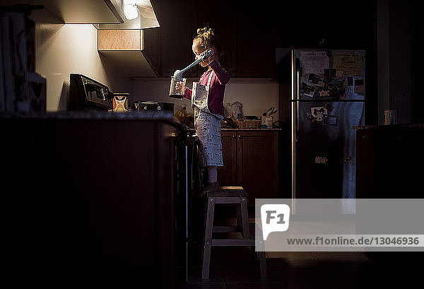 Seitenansicht eines Mädchens  das zu Hause in der Küche auf einem Hocker stehend Essen zubereitet