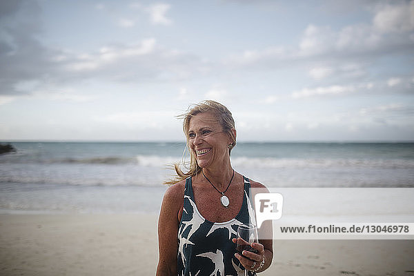 Fröhliche Frau hält Weinglas  während sie am Strand steht