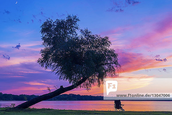 Frau entspannt sich am Seeufer vor dramatischem Himmel bei Sonnenuntergang