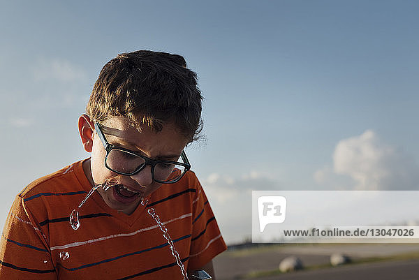 Junge trinkt Wasser aus Brunnen gegen den Himmel im Park