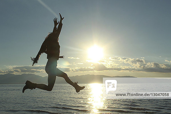 Fröhliche Frau springt am See gegen den Himmel