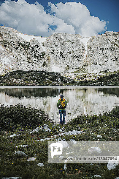 Rear view of hiker with backpack standing at lakeshore against Medicine Bow Mountains