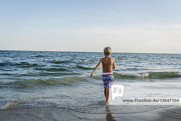 Rear view of shirtless boy walking at Tobay Beach towards sea against sky