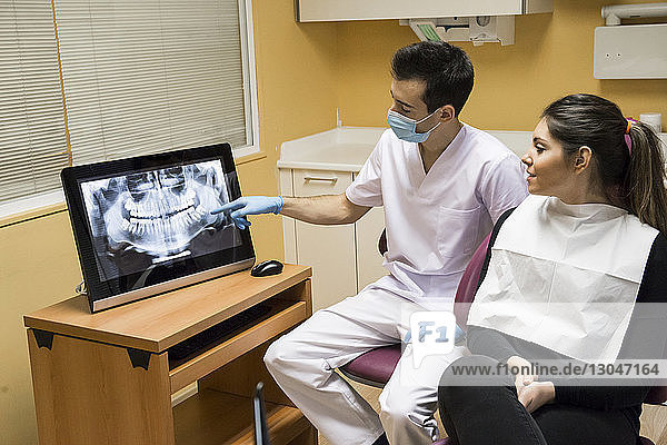 Dentist showing x-ray on desktop computer to patient while sitting in clinic