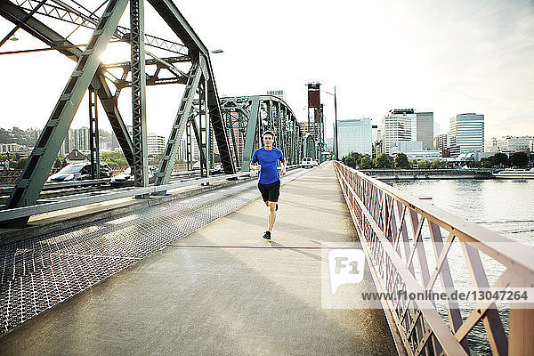 Sporty man jogging on bridge against sky