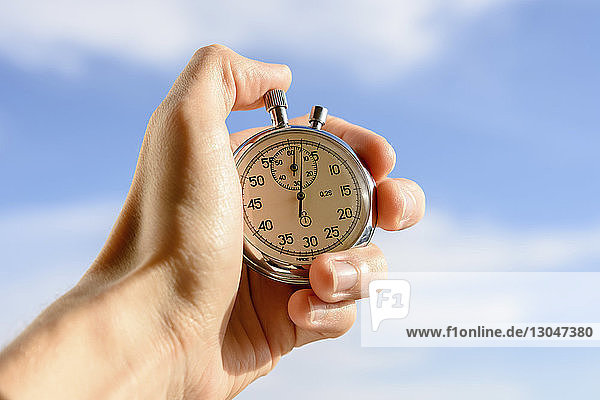 Abgehackte Hand eines Mannes der eine Stoppuhr gegen den Himmel hält