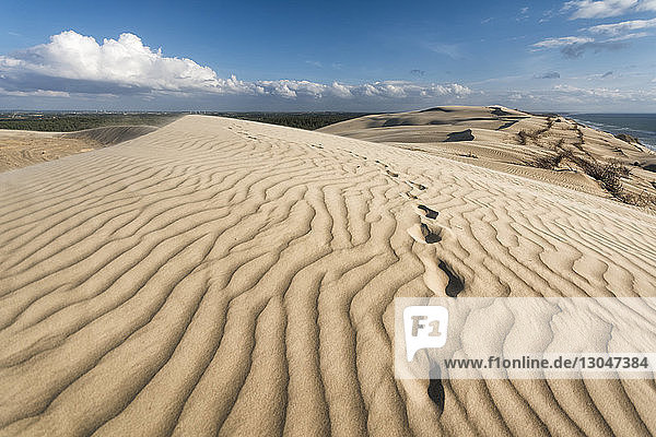 Scenic view of wave pattern on sand at beach against blue sky