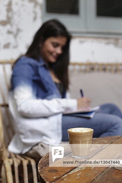 Schreibende Frau mit Kaffee auf dem Tisch im Vordergrund
