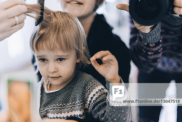 Mittelteil eines Mannes  der die Haare eines Friseurmädchens fotografiert  das mit seiner Mutter im Salon sitzt