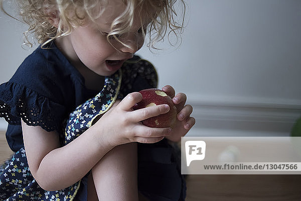 Glückliches Mädchen schaut auf den Apfel  während es zu Hause auf dem Boden sitzt