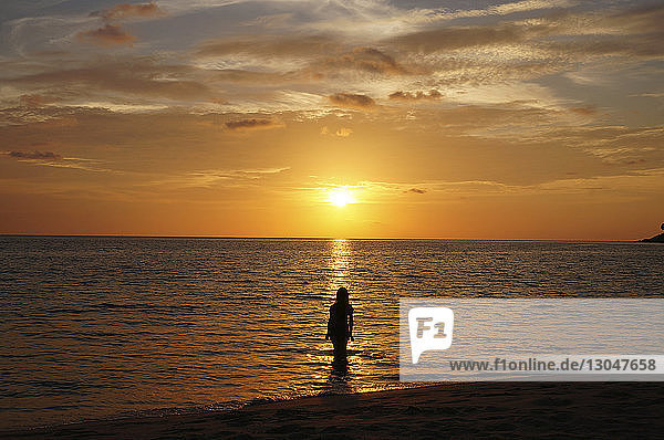 Rückansicht einer Silhouettenfrau  die bei Sonnenuntergang im Meer gegen den Himmel steht