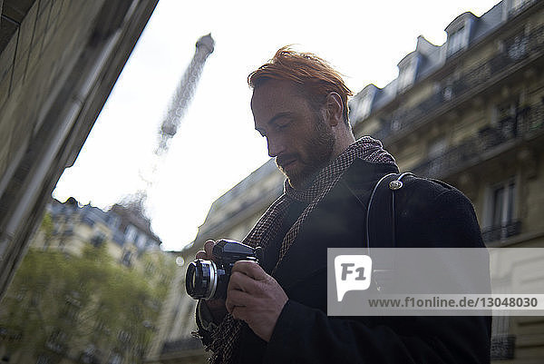 Low angle view of man watching pictures on DSLR camera against Eiffel Tower and buildings