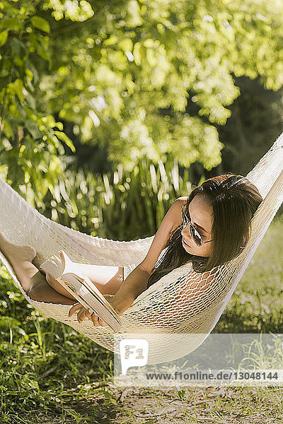 Frau liest Buch  während sie sich in der Hängematte entspannt
