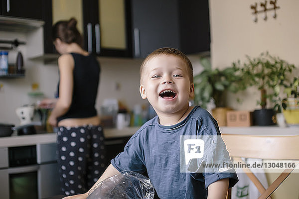 Porträt eines glücklichen Jungen mit einer Mutter  die zu Hause im Hintergrund arbeitet