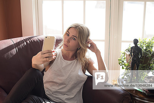 Woman taking selfie while sitting on armchair at home