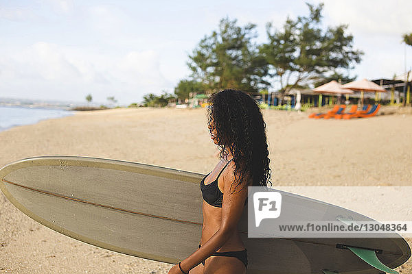 Seitenansicht einer Frau  die ein Surfbrett trägt  während sie am Strand auf Sand läuft
