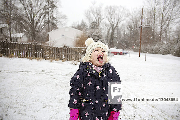 Playful girl sticking out tongue while standing on snow covered field