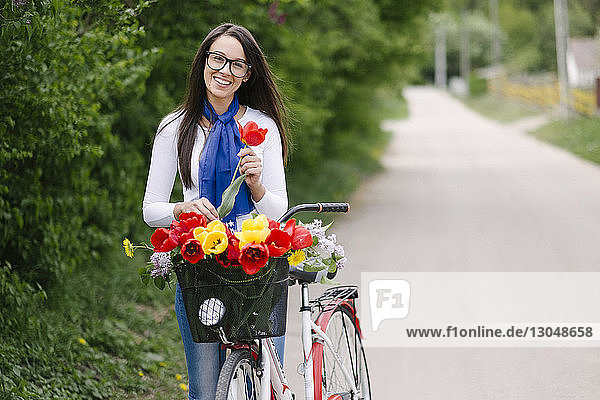 Porträt einer fröhlichen jungen Frau mit Fahrrad  die eine Tulpe auf der Strasse hält