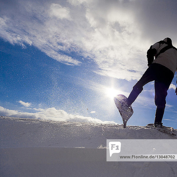 Low angle view of man snowshoeing on snow covered field against cloudy sky