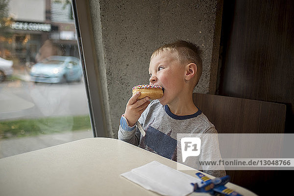 Boy eating donut while sitting at table in restaurant