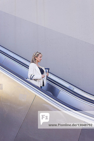 Businesswoman standing on escalator against wall in city