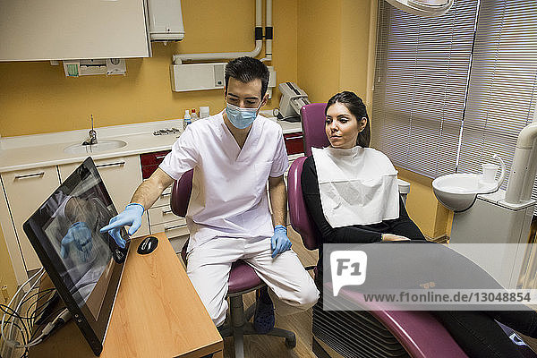 Dentist explaining x-ray report on desktop computer to patient while sitting in clinic