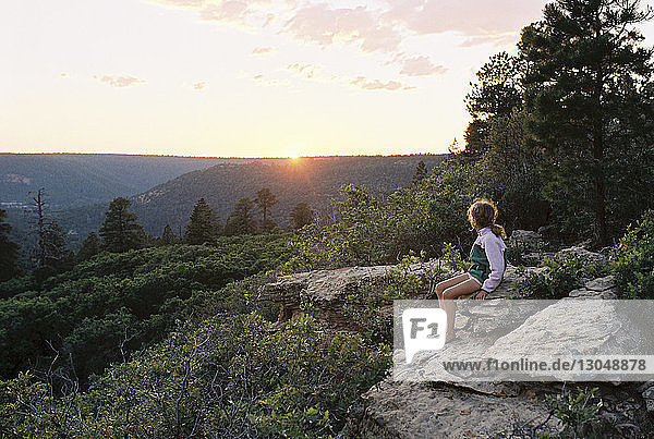 Girl looking at view while sitting on rocks during sunset