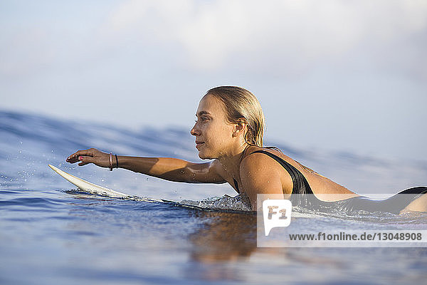 Zuversichtliche Frau liegt auf einem Surfbrett am Strand gegen den Himmel