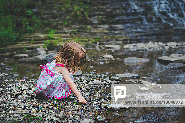 Seitenansicht eines Mädchens  das mit Kieselsteinen spielt  während es am Fluss kauert