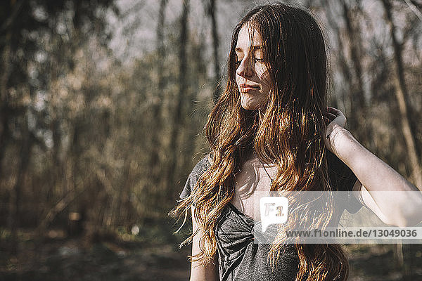 Junge Frau mit Hand im Haar steht am Wald