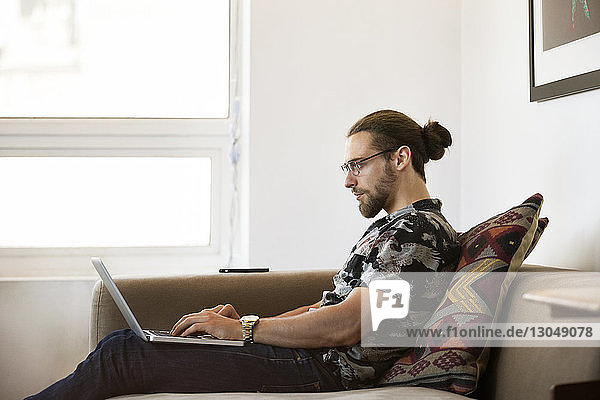 Geschäftsmann benutzt Laptop  während er im Kreativbüro auf dem Sofa sitzt