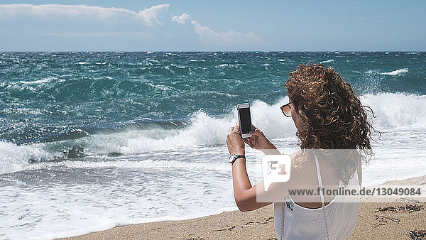Frau fotografiert im Sommer durch ein Smartphone  während sie am Ufer steht