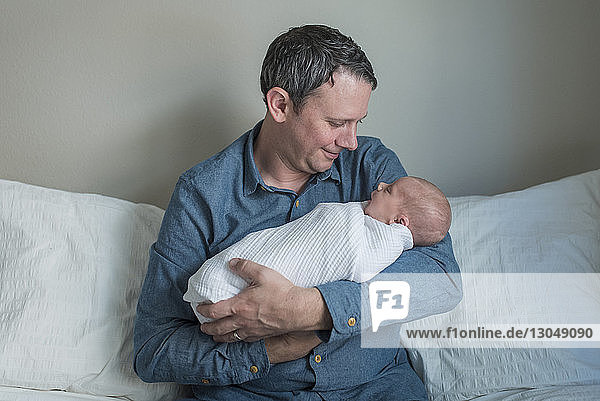 Vater trägt neugeborenen Jungen  während er zu Hause auf dem Sofa sitzt