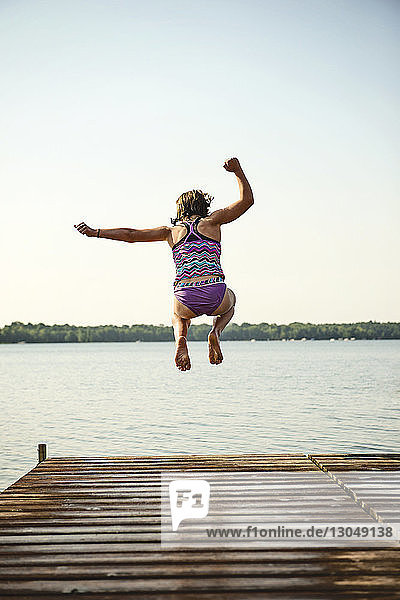 Rear view of girl jumping in lake against clear sky