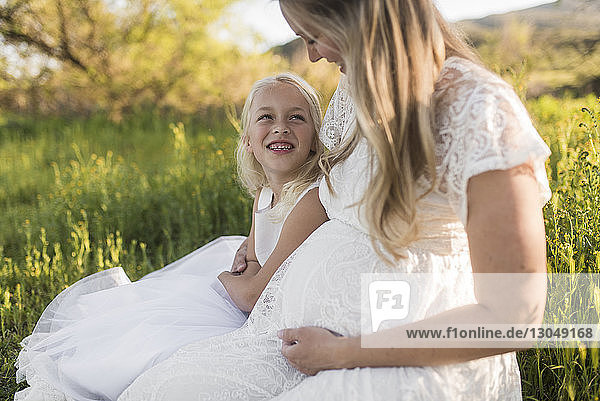 Happy mother and daughter sitting on grassy field in park