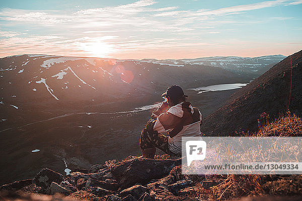 Hochwinkelansicht eines Wanderers  der bei Sonnenuntergang auf einer Klippe gegen den Himmel sitzt