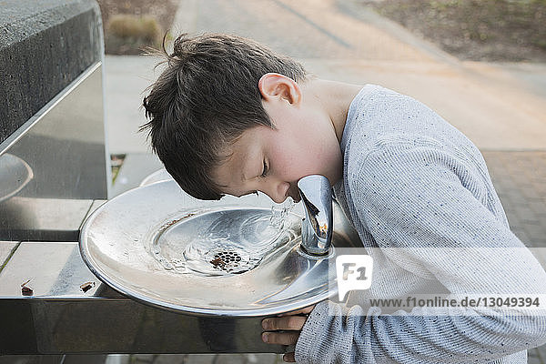 Durstiger Junge trinkt Wasser aus Brunnen im Park