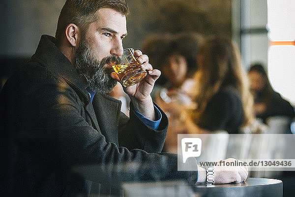 Nachdenklicher Geschäftsmann trinkt Alkohol im Hotel durch Fenster gesehen