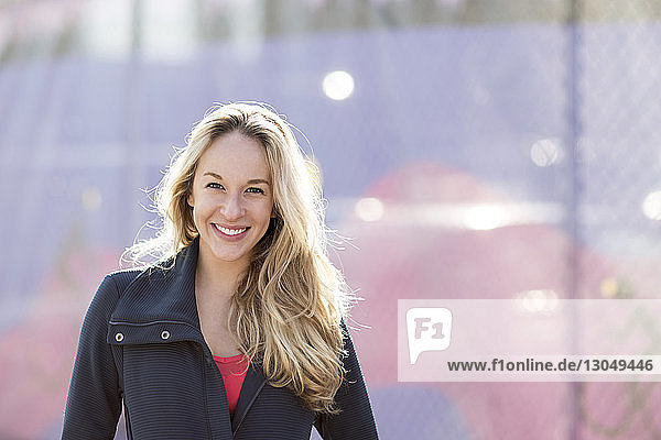 Portrait of smiling athlete standing by fence during sunny day