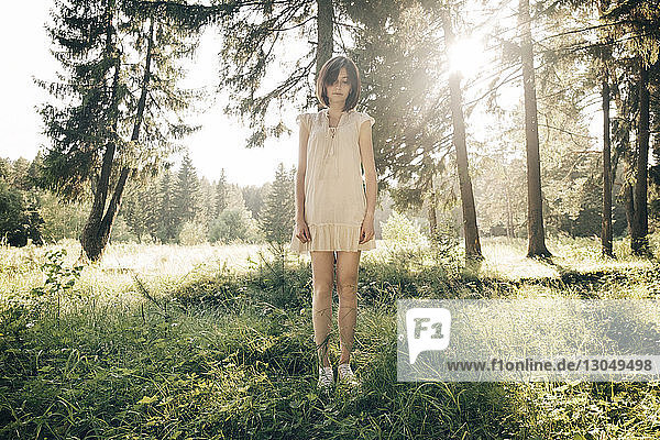 Traurige junge Frau in voller Länge auf Grasfeld im Wald stehend