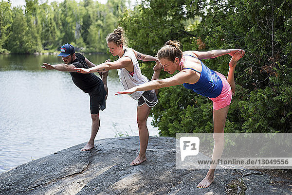Friends stretching legs while practicing yoga on rock at lakeshore