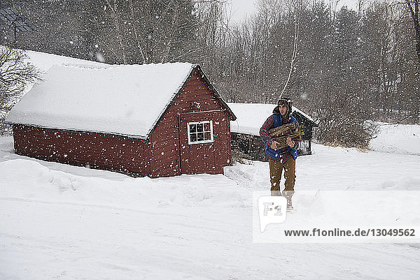 Mann trägt Brennholz  während er auf schneebedecktem Feld geht