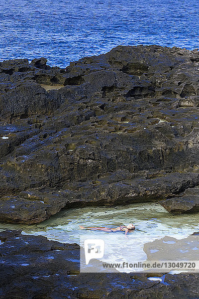 Hochwinkelaufnahme einer Bikini tragenden Frau  die an Felsen im Meer liegt