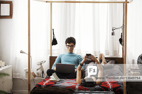 Couple using laptop and smart phone on bed at home
