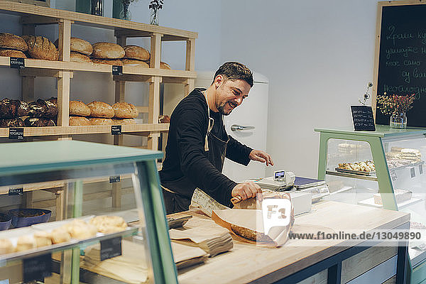 Happy owner holding paper bag while standing at counter in bakery