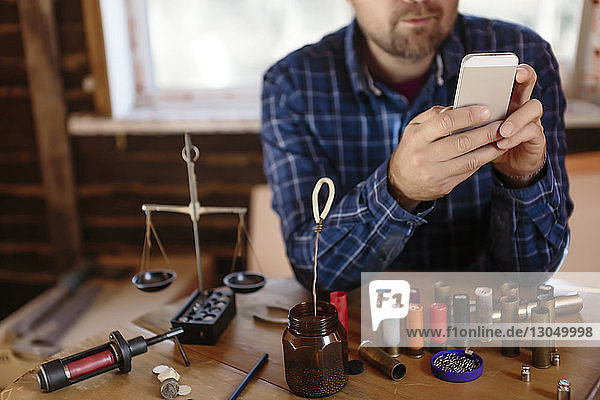 Mittelsektion eines Arbeitnehmers  der ein Mobiltelefon benutzt  während er in der Werkstatt am Tisch sitzt