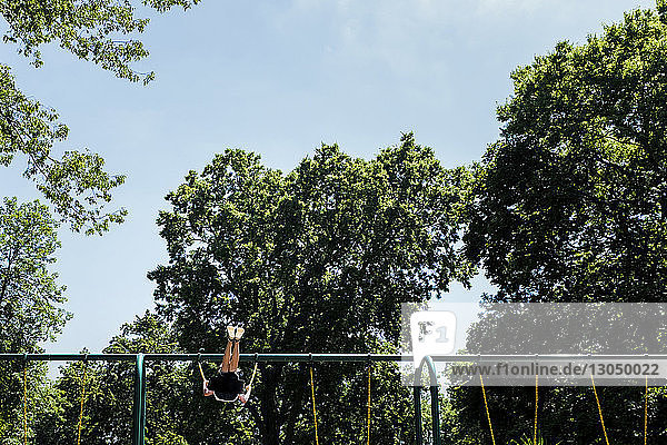 Low section of boy swinging at playground by trees against sky
