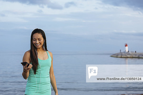 Glückliche Frau benutzt Smartphone beim Musikhören gegen das Meer