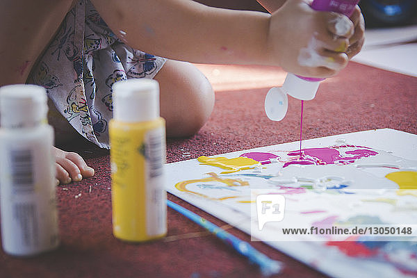 Beschnittenes Bild eines Mädchens  das zu Hause Aquarellfarben auf Papier gießt